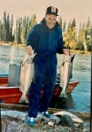 Man holding two large fish at water's edge.